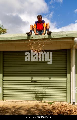 homme porte de garage sur le toit assis mains jetant quelques feuilles sur la gouttière nettoyer les gouttières du toit des débris laisse la maison boucher queensl Banque D'Images