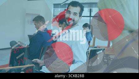 Homme mi-adulte souriant se tournant vers collègue dans la salle de conférence, avec des ordinateurs portables et des superpositions numériques Banque D'Images