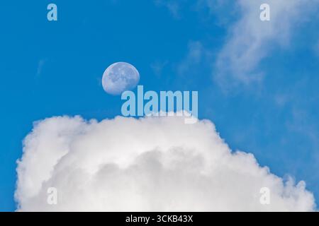 La lune capturée entre les nuages contre le ciel bleu du petit matin Banque D'Images