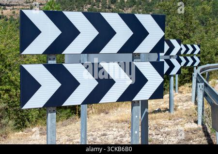 Panneaux de signalisation routière en chevron noir et blanc pointant vers la droite sur un virage montagneux prononcé. Banque D'Images