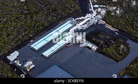 Centrale géothermique avec des structures à toiture légère, des émissions de vapeur et des canalisations, située dans un terrain volcanique mousselineux en Islande, capturée par le haut. Banque D'Images