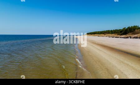 Une scène côtière sereine à Palanga avec des rives sablonneuses, des eaux turquoises et des pins verts luxuriants sous un ciel bleu clair, mettant en valeur la beauté naturelle. Banque D'Images