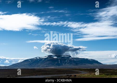 Vue d'une montagne dramatique et couvrante coiffée d'un nuage tourbillonnant sous un vaste ciel, contrastée avec le paysage serein, Blafell, Bláskógabyggð, Banque D'Images