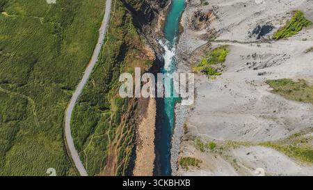 Rivière turquoise coule à travers un canyon accidenté avec une petite cascade, bordé par une végétation luxuriante d'un côté et un terrain rocheux de l'autre. Banque D'Images