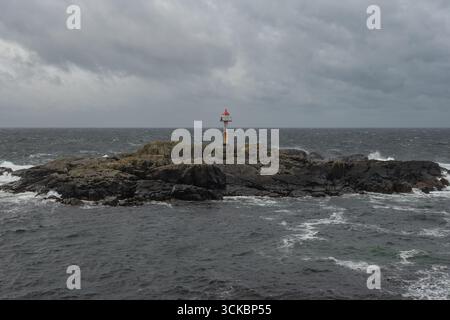 Un petit îlot rocheux avec une balise de navigation au sommet rouge se dresse au milieu des eaux sombres et agitées sous un ciel couvert le long de la côte norvégienne. Banque D'Images