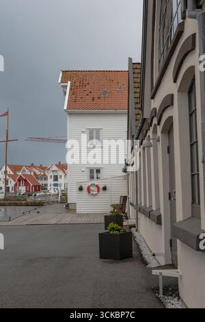 Des bâtiments traditionnels de style scandinave aux façades rouges et blanches bordent un front de mer en Norvège. Un mât de voilier en bois et une grue sont visibles à proximité. Banque D'Images
