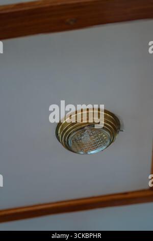 Un plafonnier en laiton avec un couvercle en verre texturé, monté sur une surface blanche avec des garnitures en bois, reflétant le design maritime traditionnel. Banque D'Images