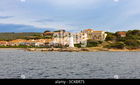 Phare d'entrée du port de Palau en Sardaigne, Italie, avec des maisons pastel, collines verdoyantes, rivage rocheux, et les eaux méditerranéennes calmes. Banque D'Images