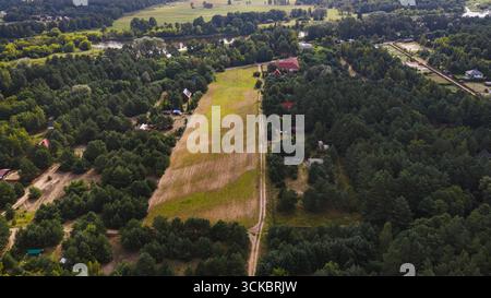 Vue par drone d'un champ étroit bordé de forêts, de maisons dispersées, de chemins de terre et d'une rivière sinueuse près de Nowy Lubiel, Pologne. Banque D'Images