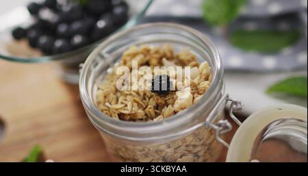 Montrant un pot en verre de granola surmonté de baies séchées sur le plan de cuisine, bol en verre de baies. Petit déjeuner, sain, rustique, naturel, bio, foodstylin Banque D'Images
