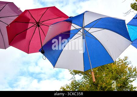 L'image montre trois parapluies vibrants suspendus à des fils à l'extérieur contre un ciel nuageux. Un parapluie a un design géométrique bleu et jaune, anot Banque D'Images