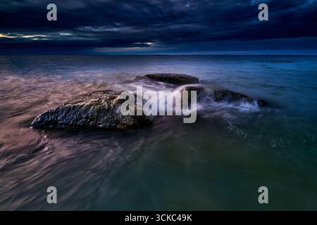 Des rochers lavés par les vagues se détachent dans la mer sous un ciel nocturne dramatique et sombre. La longue exposition crée une eau fluide et fluide et capture la tranquillité y Banque D'Images