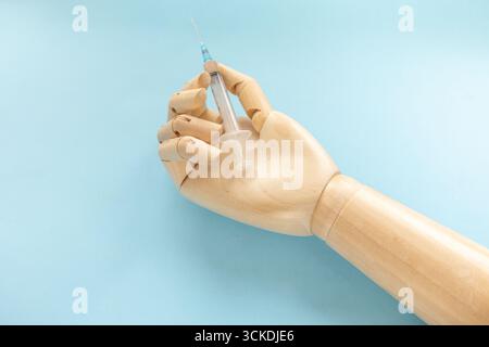 Main humaine en bois avec seringue avec vaccin pour la maladie sur fond bleu clair. Le médecin tient seringue avec injection médicale. Concept de soins de santé et de prévention des maladies Banque D'Images