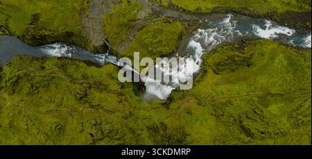 Image aérienne d'une cascade en Islande coulant à travers un terrain couvert de mousse et de roches volcaniques, avec un sentier serpentant à travers le paysage spectaculaire. Banque D'Images