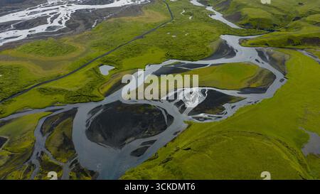 Le système fluvial tressé serpente à travers un terrain couvert de mousse avec un sol volcanique. Une route étroite traverse le paysage verdoyant de l'Islande. Banque D'Images