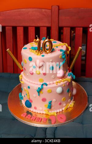 Gâteau d'anniversaire rose à deux niveaux avec pois et topper numéro dix sur fond rouge. Banque D'Images