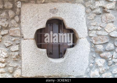 Fenêtre en forme de trèfle avec une grille en métal - Un gros plan détaillé d'une petite fenêtre en forme de trèfle avec une grille en métal serrée dans un mur de pierre antique Banque D'Images