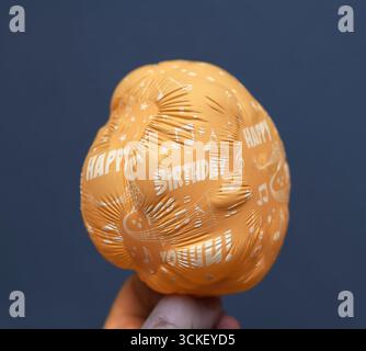 Ballon dégonflé orange avec texte joyeux anniversaire et notes de musique imprimées sur la surface tenue à la main symbolisant la déception et la fête fanée Banque D'Images