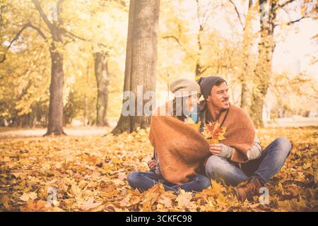 un couple amoureux assis dans les feuilles d'automne Banque D'Images