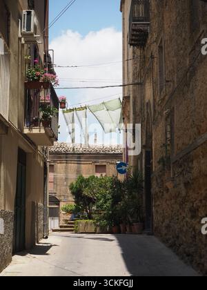 Rue étroite à Enna avec buanderie suspendue, murs en pierre, pots de fleurs et charme méditerranéen dans la ville historique sicilienne, Italie Banque D'Images