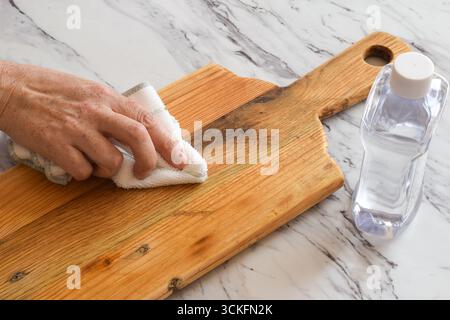 Gros plan de la main d'une femme traitant une planche à découper en bois avec de l'huile minérale. Concept d'entretien de cuisine, d'entretien du bois, d'assaisonnement et de protection à l'aide Banque D'Images