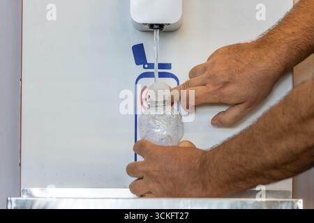 Mains masculines remplissant une bouteille en plastique à partir d'une machine distributrice d'eau Banque D'Images