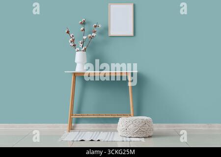 Pouf, table et vase avec des fleurs de coton près du mur vert à l'intérieur du salon Banque D'Images
