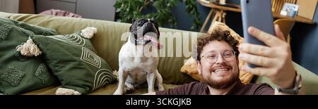 Image d'en-tête d'un jeune homme prenant Selfie avec bouledogue français assis sur un canapé Banque D'Images