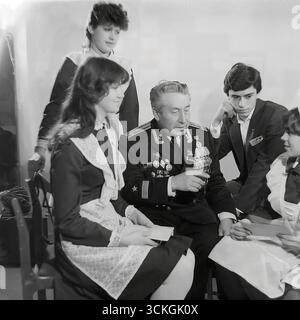 Une « réunion de générations » à l'école secondaire n ° 12 à Sloviansk à la fin des années 1970 Le voenruk (instructeur militaire) de l'école, un vétéran de la marine décoré dans son uniforme complet avec des médailles, donne une « leçon de courage » aux élèves du secondaire. Les élèves, vêtus d'uniformes scolaires soviétiques standard avec un badge Komsomol, écoutent ses histoires de guerre. Cette image est symbolique du vaste système d'éducation patriotique pour les jeunes qui était une pierre angulaire de la société en URSS pendant l'ère Brejnev Banque D'Images