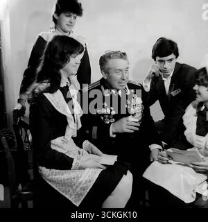 Une « réunion de générations » à l'école secondaire n ° 12 à Sloviansk à la fin des années 1970 Le voenruk (instructeur militaire) de l'école, un vétéran de la marine décoré dans son uniforme complet avec des médailles, donne une « leçon de courage » aux élèves du secondaire. Les élèves, vêtus d'uniformes scolaires soviétiques standard avec un badge Komsomol, écoutent ses histoires de guerre. Cette image est symbolique du vaste système d'éducation patriotique pour les jeunes qui était une pierre angulaire de la société en URSS pendant l'ère Brejnev Banque D'Images