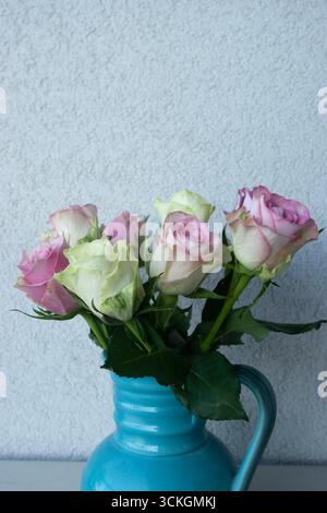 Bouquet de roses roses et blanches dans un vase en céramique bleue sur un fond mural texturé Banque D'Images