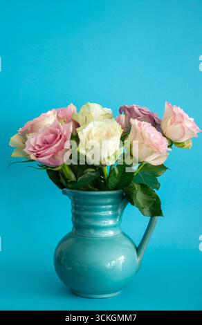 Bouquet de roses roses et blanches dans un vase en céramique bleue sur un fond mural texturé Banque D'Images