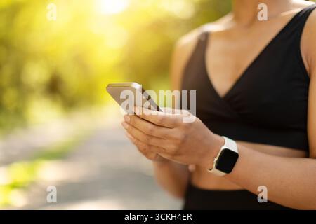 Gros plan sur les mains de femmes afro-américaines tenant un smartphone pendant l'entraînement en extérieur Banque D'Images
