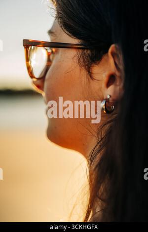 Jeune femme portant des lunettes profitant de la lumière dorée du soleil au coucher du soleil Banque D'Images