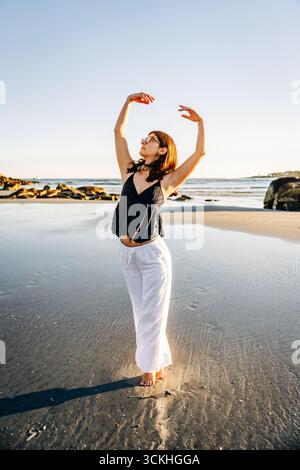 Jeune femme pratiquant le ballet pose sur la plage de sable au coucher du soleil Banque D'Images Jeune femme pratiquant le ballet pose sur la plage de sable au coucher du soleil Banque D'Images