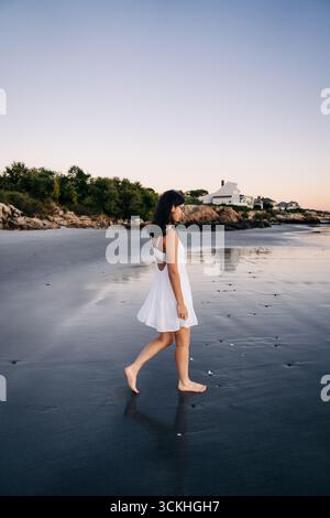 Jeune femme marchant pieds nus sur la plage au coucher du soleil Banque D'Images
