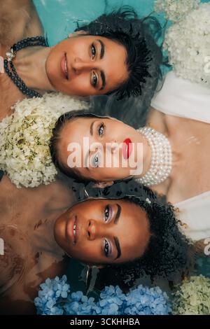 Trois femmes diverses flottant dans l'eau avec des fleurs et des bijoux Banque D'Images