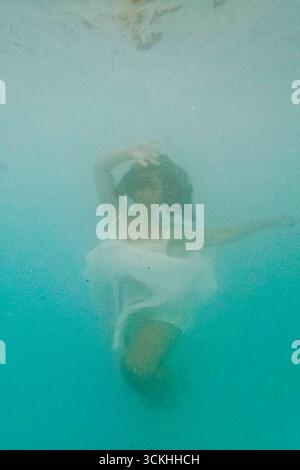 Femme portant une robe blanche flottant sous l'eau dans l'eau turquoise Banque D'Images