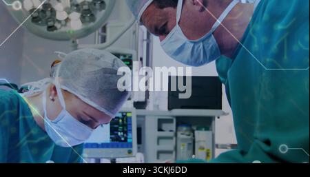 Chirurgiens penchants dans les gommages pratiquant une intervention chirurgicale au BLOC OPÉRATOIRE, avec plafonnier et moniteur vital Banque D'Images