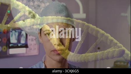 Médecin debout portant des gommages bleu clair avec bonnet chirurgical dans la salle de traitement, avec recouvrement d'ADN Banque D'Images