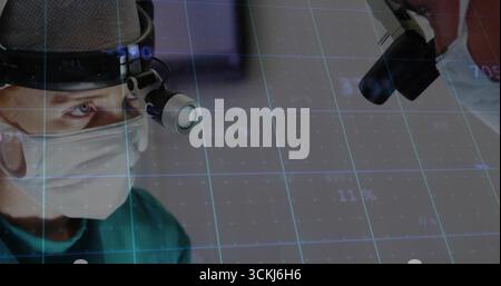 Chirurgien de sexe masculin portant une blouse verte focalisant le regard sur le dispositif d'imagerie dans OU, avec superposition de grille numérique Banque D'Images