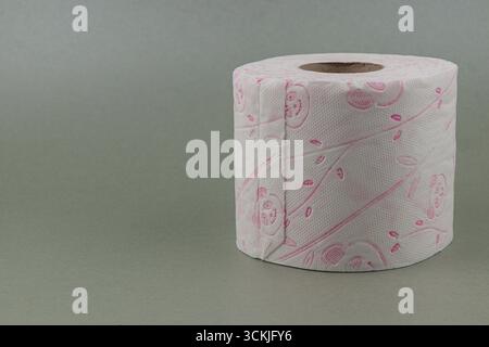 Ukraine Lviv 15.08.25 Une vue rapprochée d'un rouleau de papier toilette décoratif avec un motif floral, placé sur un fond gris doux, mettant en valeur son Banque D'Images