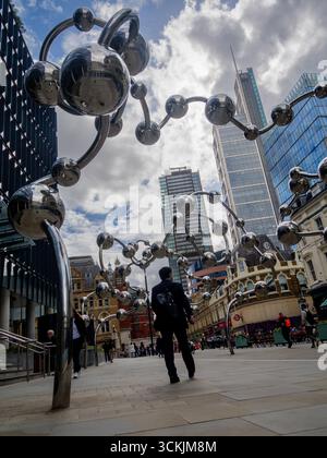 Les piétons passent devant Infinite accumulation de Yayoi Kusama, commandée par la fondation artistique crossrail à l'extérieur du 100 Liverpool Street London UK, avec des gratte-ciel en arrière-plan sur un ciel sombre Banque D'Images