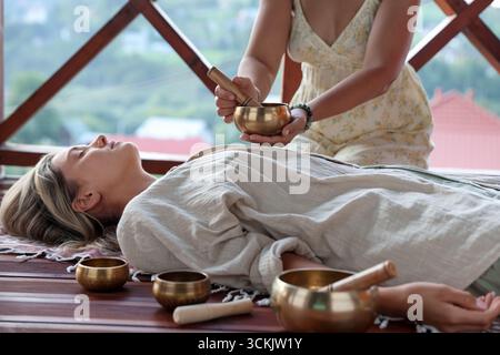 Femme subissant une thérapie de bol chantant couchée sur le sol à l'intérieur Banque D'Images