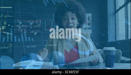 Examen de documents imprimés, gestes sur un ordinateur portable au bureau, dans un blazer brun avec des graphiques numériques Banque D'Images