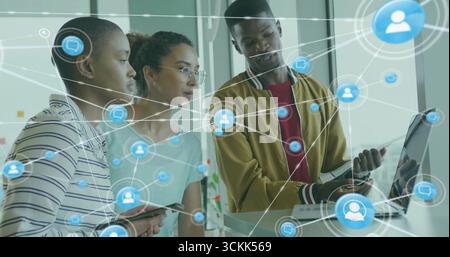 Trois collègues examinant l'ordinateur portable au bureau debout dans le bureau, avec des icônes de réseau de tablette smartphone Banque D'Images