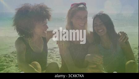 Rire trois amies femmes dans des hauts sans manches et des lunettes de soleil, assis sur la plage avec les vagues de l'océan Banque D'Images