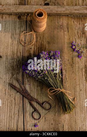 Bouquet de lavande séchée avec des ciseaux et de la ficelle sur une surface en bois rustique, nature morte artisanale à base de plantes. Banque D'Images