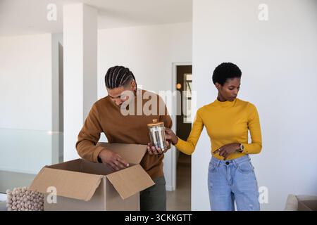Couple diversifié déballage de la boîte en carton dans le salon moderne avec pot en verre et couvercle en bois Banque D'Images