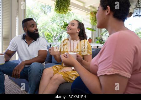 Divers amis discutant sur des tasses à café et assis sur un canapé sur le porche avec des jardinières suspendues Banque D'Images